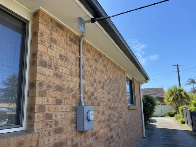 Overhead service cable and point-of-attachment bracket on a brick house exterior in Long Jetty
