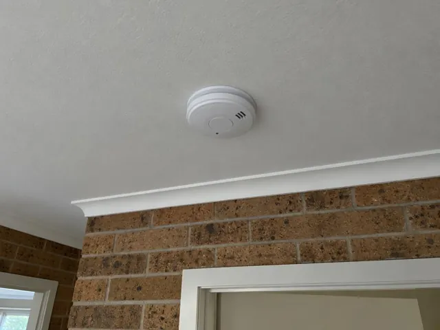 Ceiling smoke alarm on a white ceiling above a brick wall and doorway in The Entrance
